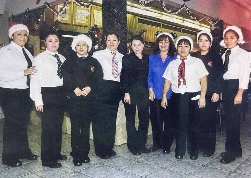 Eight female restaurant staff members in uniform and festive hats pose for a group photo.