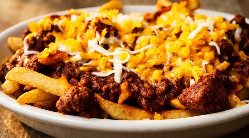 Close-up of golden french fries smothered in chili and topped with shredded cheddar and Monterey Jack cheese.
