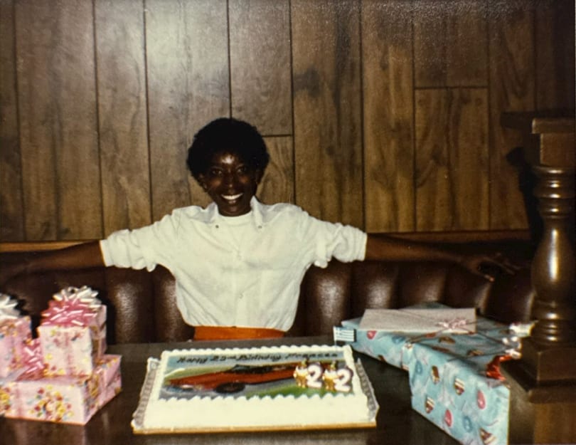 Smiling person celebrating a 22nd birthday with cake and presents at a restaurant booth.